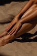 © Mirrorstudio - Sunlit female legs on sandy beach. Skin care, sun protection