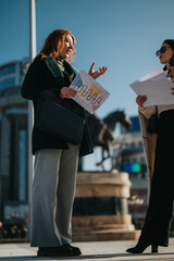 Wall Mural - Two businesswomen analyzing data and collaborating on a project plan in an outdoor setting.