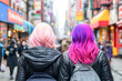 © Kowit - Two friends with colorful hair walking in a vibrant city street.