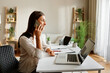 © djile - Young businesswoman working from home office using laptop and talking on mobile phone