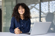 © Liubomir - Successful and joyful businesswoman at workplace inside office smiling and looking at camera. Satisfied woman working at desk with laptop.