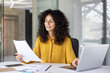 © Liubomir - Successful and joyful woman at workplace checking financial reports and contracts. Businesswoman doing paperwork inside office, using laptop. Financier preparing and filling out tax forms.