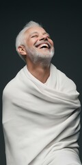 Wall Mural - A man with white hair is wearing a white towel and smiling. He is sitting on a surface and he is enjoying himself