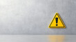 © Bonsales - Warning sign with yellow triangular shape displaying exclamation mark, mounted on concrete wall, casting reflection on white floor surface