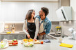 © unai - Happy couple preparing vegetable salad, embracing and laughing in modern kitchen