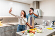 © unai - Happy couple making video call while preparing vegetables in modern kitchen