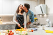© unai - Happy couple preparing dinner together, embracing and smiling in modern kitchen