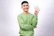 © Daniel - An Asian man in a green sweatshirt is smiling while holding up four fingers on his right hand. His left arm is crossed, and he stands against a white background, expressing confidence and enthusiasm