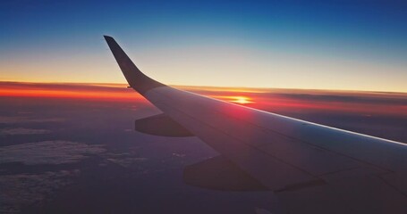 Wall Mural - Flying with airplane over sunset horizon with clouds and land below