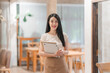 © Kritdanai - Smiling Waitress in Cafe: A warm and inviting portrait of a smiling waitress standing in a charming cafe, ready to serve with professionalism and a friendly demeanor.