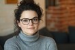 © Velar - Detailed close-up of an attractive woman with big green eyes, full lips, smooth skin, and a fair-haired ponytail, adorned with large glasses and a casual gray sweater, separated from a brick wall