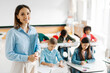 © Home-stock - Portrait of friendly European teacher standing in classroom during lesson with pupils studying on background, children writing test
