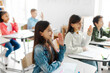 © Home-stock - Positive preteen students with raised hands, sitting at desks in classroom in private school, participating at interesting lesson