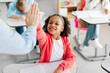 © Home-stock - Little black schoolgirl giving high five to teacher and smiling. Students with goals, celebration at school desk