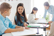 © Home-stock - European schoolgirl helping her classmate boy and pointing at his copybook, sitting at desks in classroom during lesson in private school