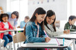 © Home-stock - Positive European school girls sitting at desks, writing in copybooks and smiling, studying together at private school