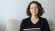 © Lerson - young woman in casual attire sits on sofa, smiling while holding tablet, exuding relaxed and confident vibe