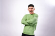 © Daniel - confident Asian man in a green sweatshirt crosses his arms and looks serious with a strong expression. He stands against a plain white background, conveying authority