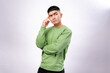 © Daniel - An Asian man in a green sweatshirt poses thoughtfully with a finger on his temple and a serious expression. He stands against a plain white background, conveying deep thinking, focus