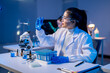 A woman in a lab coat is holding a test tube and wearing safety goggles