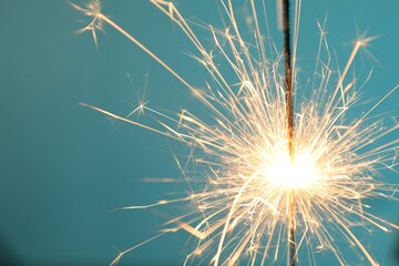 Sticker - Bright burning sparkler on light blue background, closeup