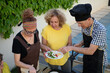 © Antonio - Close-up of three adults preparing a homemade meal outdoors, assembling tortillas with grilled vegetables and fresh salad while enjoying a casual backyard gathering in a friendly atmosphere