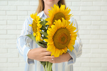 Canvas Print - Woman with beautiful sunflowers on light brick background