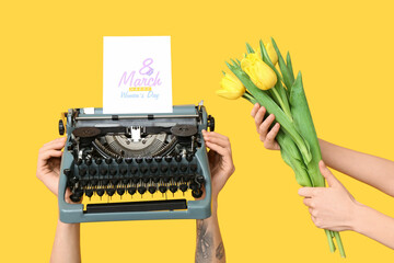 Wall Mural - Hands holding vintage typewriter, tulips and festive postcard with text 8 MARCH HAPPY WOMEN'S DAY on yellow background