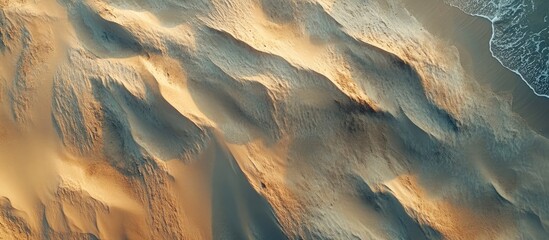 Aufkleber - Aerial view of textured sandy terrain showcasing warm golden and beige tones with gentle wave patterns along the shore against a blue ocean backdrop