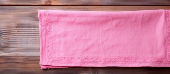 Leinwandbilder - Top view of a folded pink kitchen towel on a rustic wooden table with warm brown tones, leaving space for text on the right side.