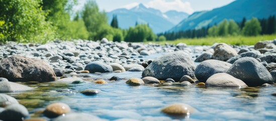 Leinwandbilder - Clear mountain river with smooth pebbles in foreground, lush greenery on banks, while majestic mountains rise in background under blue sky.