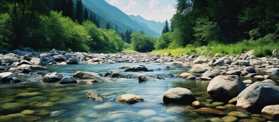 Aufkleber - Tranquil mountain river winding through lush greenery with smooth stones in the foreground and majestic peaks under a bright blue sky