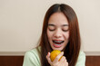 © Ekkasit A Siam - Beautiful Asian girl on vacation. Young woman with long brown hair and braces wearing light green sweater enjoying fresh fruit. orange in hand with joyful expression. Indoor setting with warm lighting