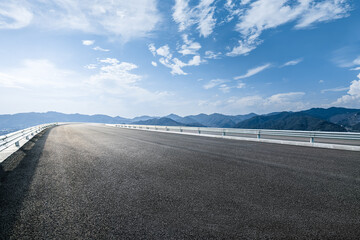 Wall Mural - Empty asphalt road leading toward mountain range under a blue sky