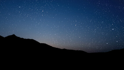 Wall Mural - A movement of stars in the night sky with the view of mountains..