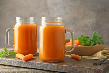 Wall Mural - Fresh carrot juice in mason jars, vegetables and mint on wooden table against gray background