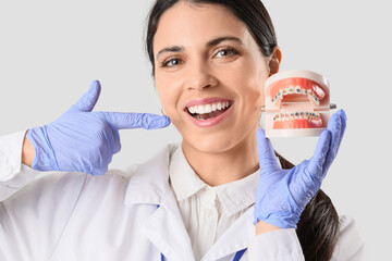 Wall Mural - Female dentist holding jaw model with braces on light background, closeup