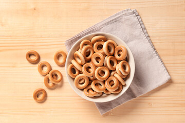 Wall Mural - Bowl of tasty bagels with napkin on light wooden background