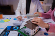 © Tj - Real estate agent showing house model to client holding money during financial meeting with charts and calculator on table, discussing housing investment and mortgage contract