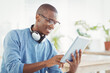 © WavebreakMediaMicro - African American man using tablet with headphones, smiling and working at office