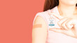 © Orawan - International HPV awareness day concept. Woman holding HPV vaccine vial while showing vaccinated arm with medical adhesive bandage strip after vaccine injection over pink background.