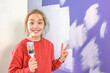 © kinovo - Positive teenage girl painting walls with a brush on a painted wall background. Space for copy