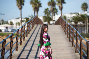 Wall Mural - Latin woman, brunette, with flowing hair, dancing flamenco on a wooden catwalk by the seashore. The woman is wearing a white dress with a floral print and ruffles. Intangible Cultural Heritage.