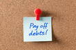 © A2Z AI  - Debt payoff reminder. A sticky note pinned to a corkboard with the handwritten message: 'Pay off debts!' A visual cue for financial goals and money management.