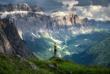 Wall Mural - sporty woman standing on a grassy hilltop with stunning view of the alpine mountains at sunset in su
