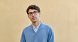 © Postmodern Studio - Young caucasian male wearing glasses and blue sweater against beige background
