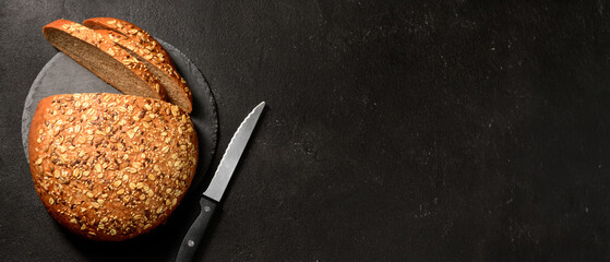 Canvas Print - Board with sliced loaf of bread and knife on black background