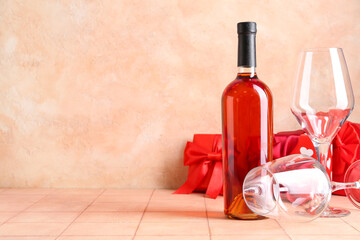 Wall Mural - Bottle of wine with glasses and gifts on beige tile table against grunge background. Valentine's Day celebration