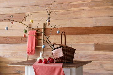 Canvas Print - Basket with tree branches, Easter eggs and apples on table near wooden wall in room