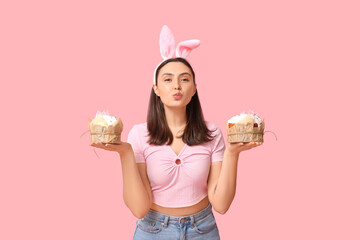 Canvas Print - Beautiful young woman in bunny ears with sweet Easter cakes on pink background